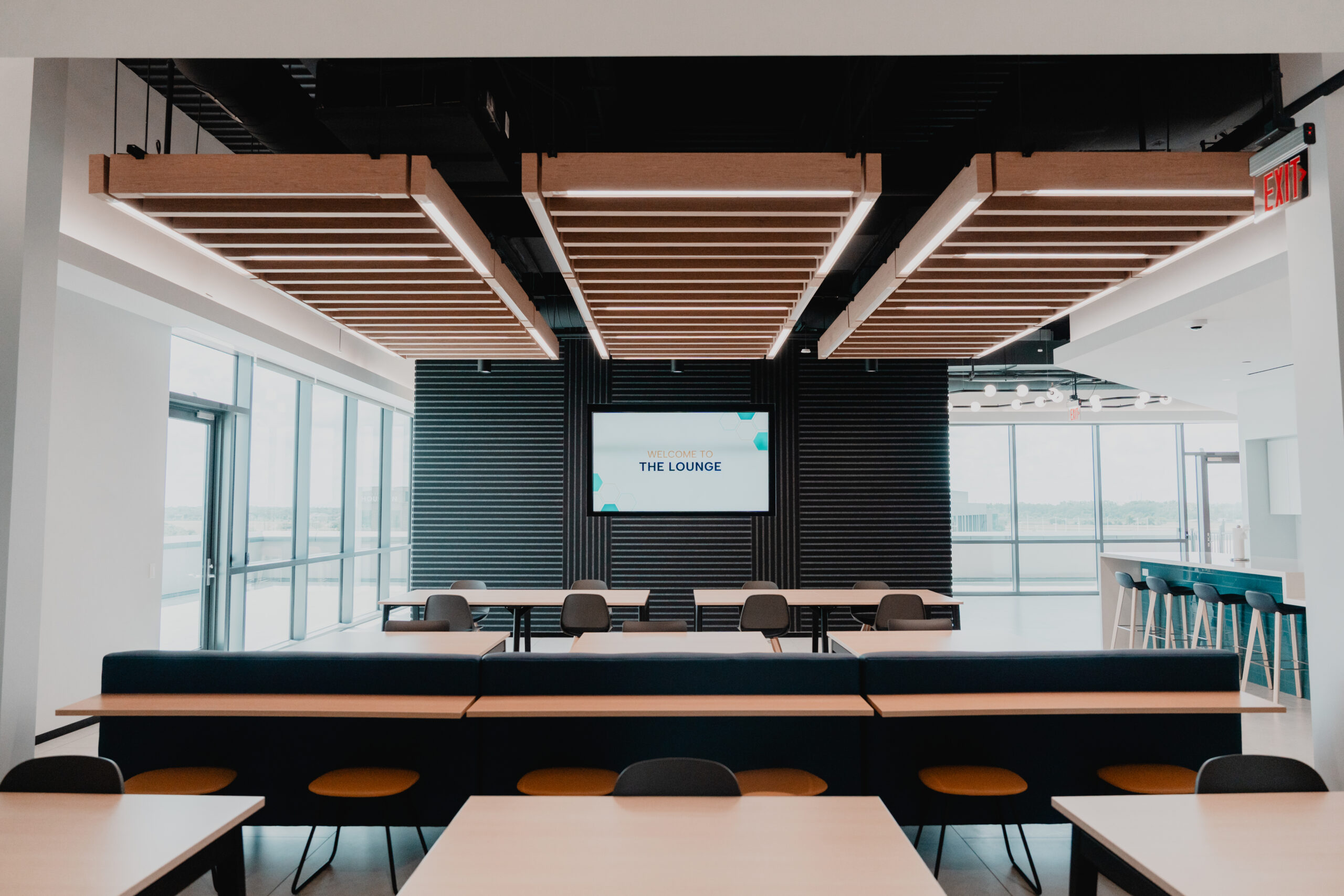 Interior lounge area at Modisoft headquarters featuring floor-to-ceiling windows, modern wood ceiling accents, and a welcome display screen.