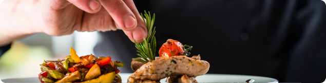 Chef garnishing a plated dish with vegetables and herbs during food preparation.