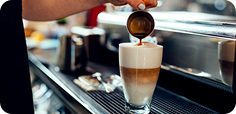 Coffee beverage being prepared as espresso is poured into a layered latte at a café workstation.