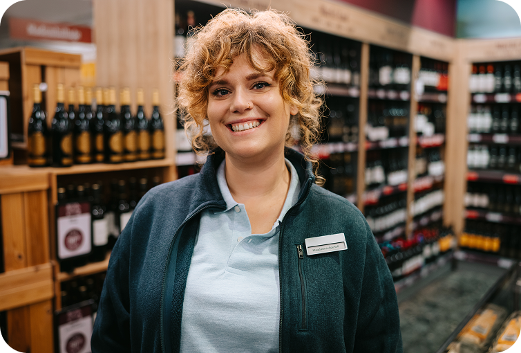 Store employee standing in a liquor store aisle surrounded by wine and beverage shelves, highlighting product organization and inventory management.